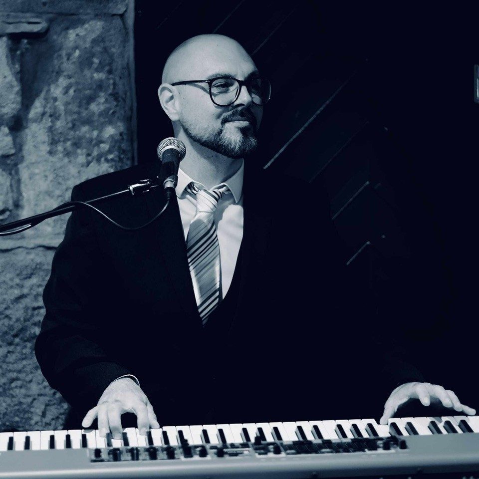 Dan Burnett is a British singer, pianist and songwriter, a two-time British Blues Awards finalist and resident performer at Grantley Hall. His music has been played on BBC Radio 2 and featured by BBC Introducing, as well as appearing internationally on film and television, including the US series Supernatural and the Nicolas Cage film Stolen.
Across more than 20 years as a professional musician, Dan has performed throughout the UK, USA and Europe — including a solo tour of New York, headline festival appearances in France and major European blues festivals. He has performed to audiences of up to 20,000, and worked alongside musicians from Robbie Williams, Tears for Fears, Status Quo and Simple Minds, as well as BAFTA and Emmy-winning composer John Altman, Queen’s Roger Taylor and Dire Straits’ John Illsley.
